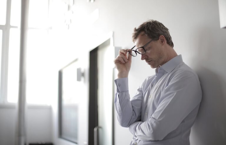 alt="a stressed man holding his eyeglass"